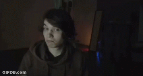 A Young Man Is Holding A Piece Of Paper And A Pen In A Dark Room . GIF