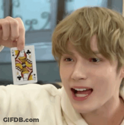 A Young Man Is Holding A Playing Card In His Hand And Pointing It At The Camera . GIF
