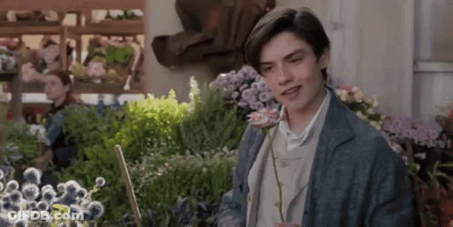 A Young Man Is Holding A Rose In A Garden GIF