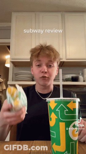 A Young Man Is Holding A Sandwich And A Subway Cup GIF