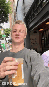 A Young Man Is Holding A Starbucks Cup In Front Of A Building GIF
