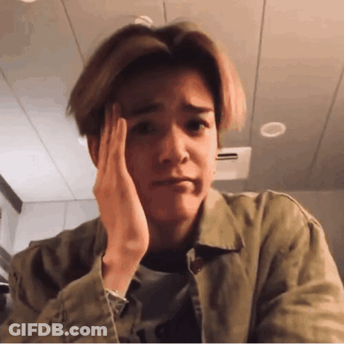 A Young Man Is Holding His Hand To His Forehead And Making A Sad Face . GIF