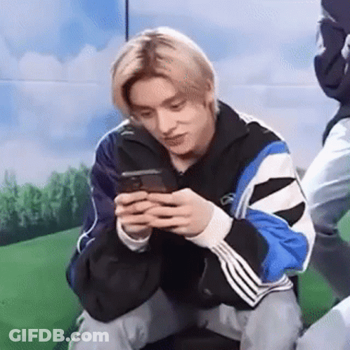 A Young Man Is Kneeling Down While Looking At His Cell Phone . GIF