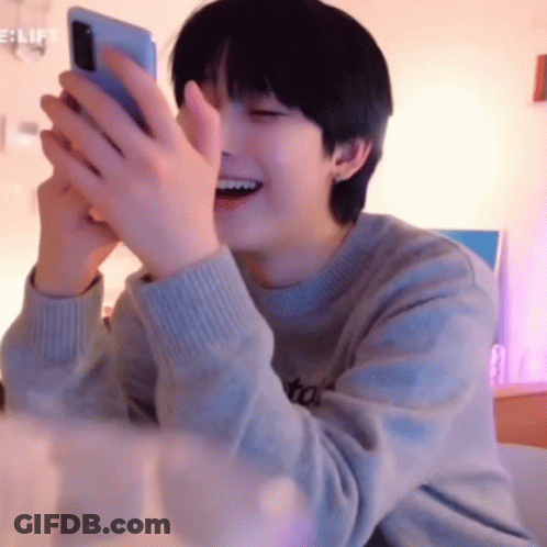 A Young Man Is Laughing While Holding A Cell Phone . GIF