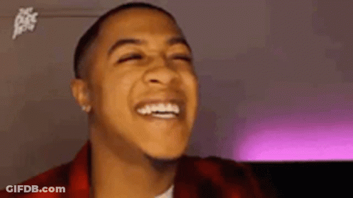 A Young Man Is Laughing With His Eyes Closed And Wearing A Red Plaid Jacket . GIF