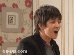A Young Man Is Laughing With His Mouth Open In A Room With Pictures On The Wall . GIF