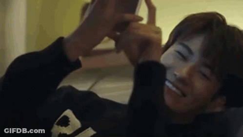A Young Man Is Laying On A Bed Taking A Selfie With His Phone . GIF