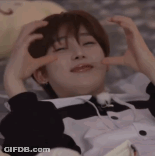 A Young Man Is Laying On A Bed With His Eyes Closed And Making A Heart Shape With His Hands . GIF
