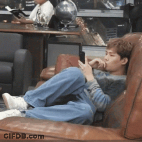 A Young Man Is Laying On A Couch Looking At His Phone GIF