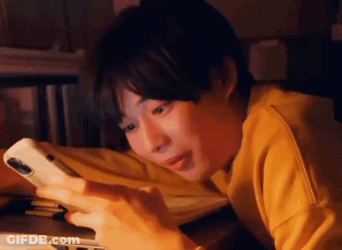 A Young Man Is Laying On His Stomach Looking At His Cell Phone . GIF
