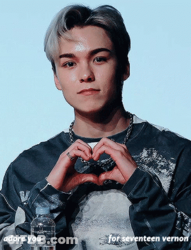 A Young Man Is Making A Heart Shape With His Hands While Holding A Bottle Of Water GIF