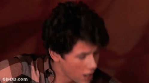 A Young Man Is Playing A Guitar In Front Of A Large Red Object GIF