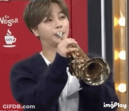 A Young Man Is Playing A Trumpet In A Room . GIF