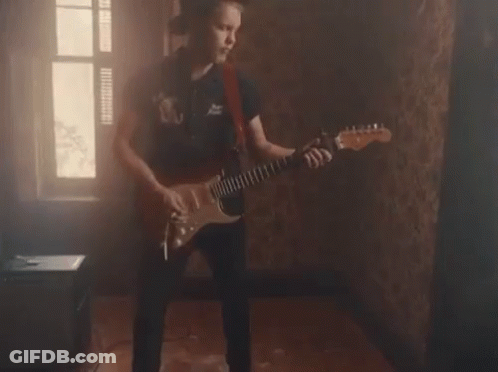 A Young Man Is Playing An Electric Guitar In A Dark Room . GIF