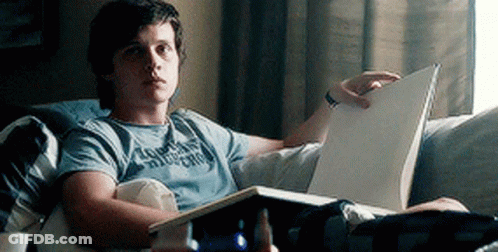 A Young Man Is Reading A Book While Laying On A Couch . GIF