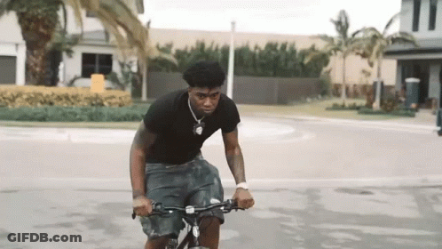 A Young Man Is Riding A Bicycle Down A Street . GIF