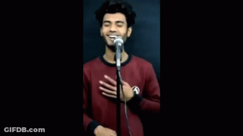 A Young Man Is Singing Into A Microphone While Holding His Hand To His Chest . GIF