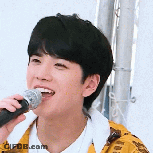 A Young Man Is Singing Into A Microphone While Wearing A Yellow Jacket . GIF