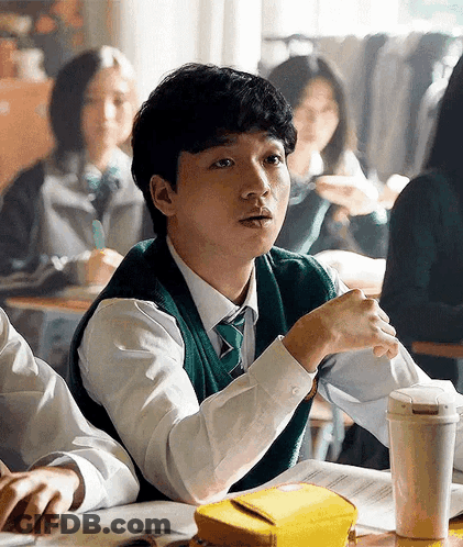 A Young Man Is Sitting At A Desk In A Classroom . GIF