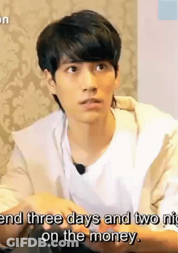 A Young Man Is Sitting At A Table And Talking To Someone While Wearing A White Shirt And A Tan Jacket . GIF