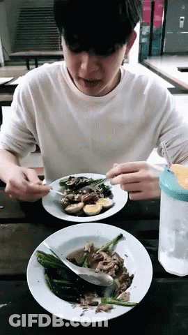 A Young Man Is Sitting At A Table Eating A Plate Of Food GIF