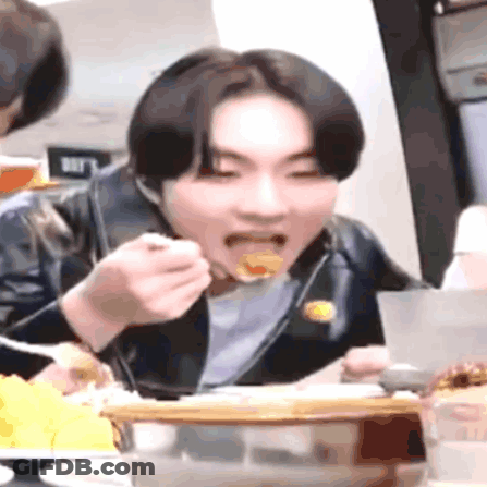 A Young Man Is Sitting At A Table Eating Food With A Fork And Spoon . GIF