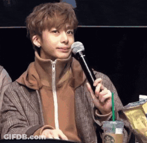 A Young Man Is Sitting At A Table Holding A Microphone And A Cup Of Starbucks Coffee . GIF