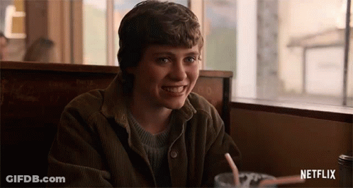 A Young Man Is Sitting At A Table In A Diner With A Drink And Smiling . GIF