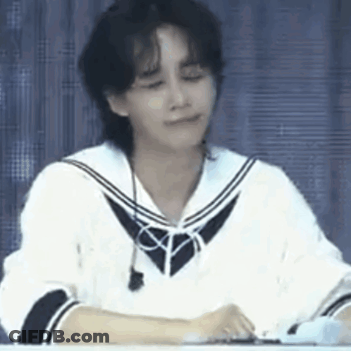 A Young Man Is Sitting At A Table With His Eyes Closed And Wearing A Sailor Uniform . GIF