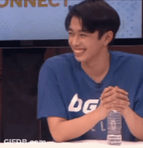 A Young Man Is Sitting At A Table With His Hands Folded And Smiling . GIF