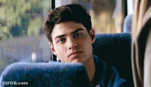 A Young Man Is Sitting In A Blue Seat On A Bus And Looking Out The Window . GIF
