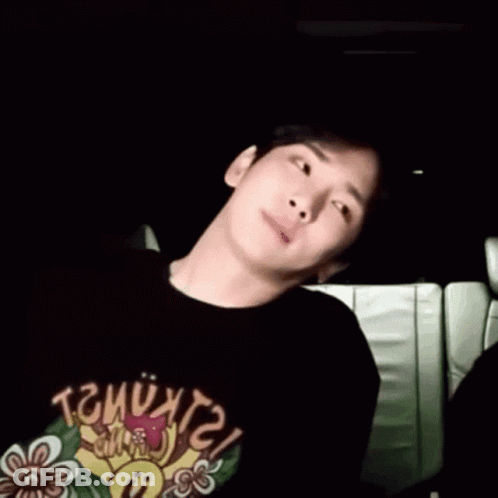 A Young Man Is Sitting In A Car Wearing A Black T-Shirt With A Flower On It . GIF