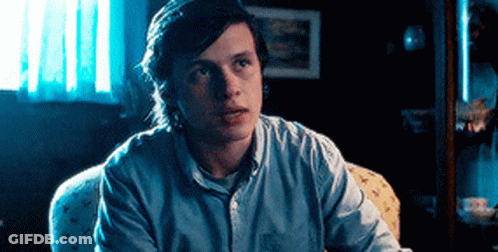 A Young Man Is Sitting In A Chair In A Dark Room Looking At The Camera . GIF
