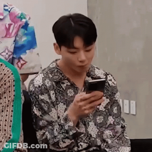 A Young Man Is Sitting In A Chair Looking At His Cell Phone . GIF