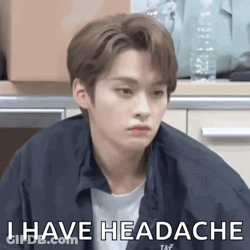A Young Man Is Sitting In A Kitchen And Making A Funny Face And Saying `` I Have Headache '' . GIF