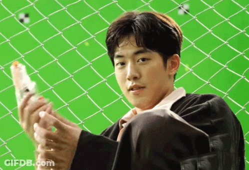A Young Man Is Sitting In Front Of A Chain Link Fence Holding A Bottle Of Water . GIF