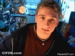 A Young Man Is Sitting In Front Of A Computer Screen And Looking At The Camera While Wearing A Necklace . GIF