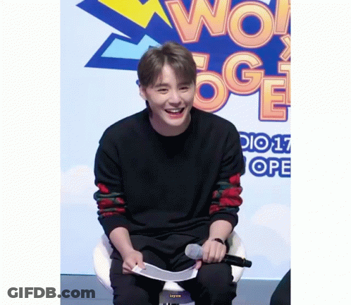 A Young Man Is Sitting In Front Of A Sign That Says Wow Oge GIF