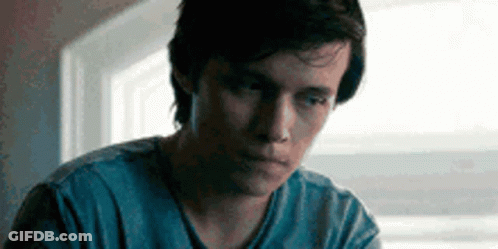 A Young Man Is Sitting In Front Of A Window Wearing A Blue Shirt . GIF