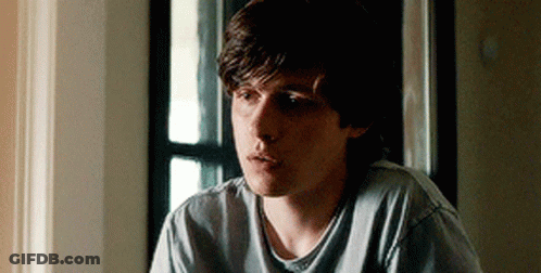 A Young Man Is Sitting In Front Of A Window Wearing A Grey Shirt . GIF