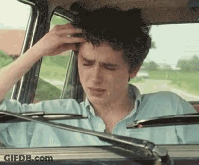 A Young Man Is Sitting In The Driver 'S Seat Of A Car Holding His Head . GIF