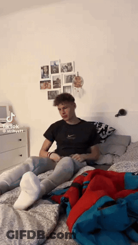 A Young Man Is Sitting On A Bed Wearing White Socks And Jeans . GIF