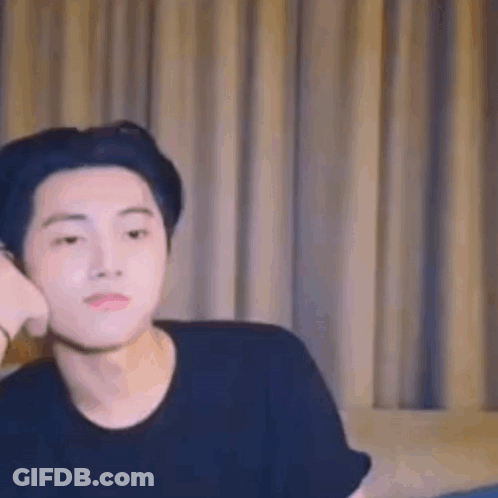 A Young Man Is Sitting On A Couch In Front Of A Window . GIF