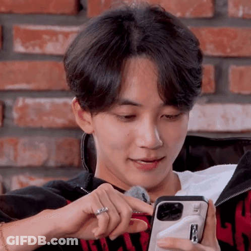A Young Man Is Sitting On A Couch Looking At A Cell Phone GIF