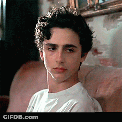 A Young Man Is Sitting On A Couch Wearing A White Shirt And Looking At The Camera . GIF