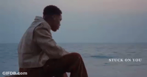 A Young Man Is Sitting On A Rock Near The Ocean . GIF