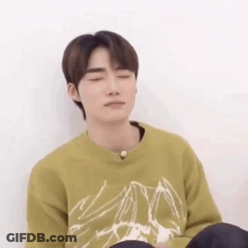 A Young Man Is Sitting On The Floor With His Eyes Closed And Wearing A Green Sweater . GIF