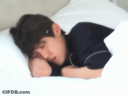 A Young Man Is Sleeping On A Bed With A Headband That Says ` ` N ` ` On It . GIF