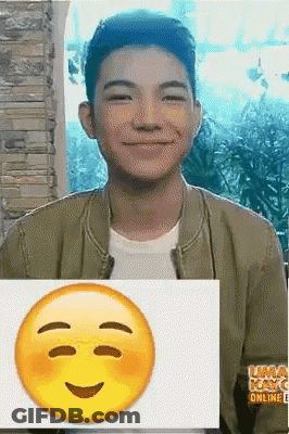 A Young Man Is Smiling And Holding A Picture Of A Smiley Face GIF
