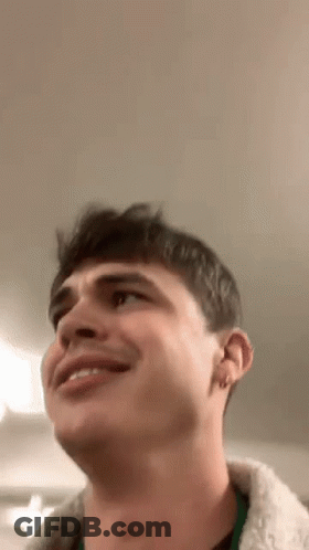 A Young Man Is Smiling And Looking Up At The Ceiling While Wearing A Fur Coat . GIF